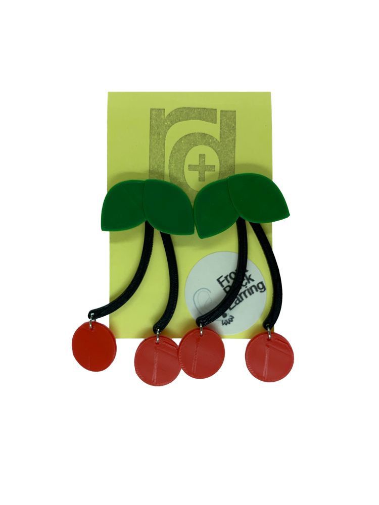 Hanging off of a yellow earring card are two statement earrings shaped like cherries. They have green leaves that are worn on the front of the ear lobe with two black stems that lead to bright red cherries. The stem is worn behind the ear to give depth to this classic style that will match any picnic or rock a billy outfit.