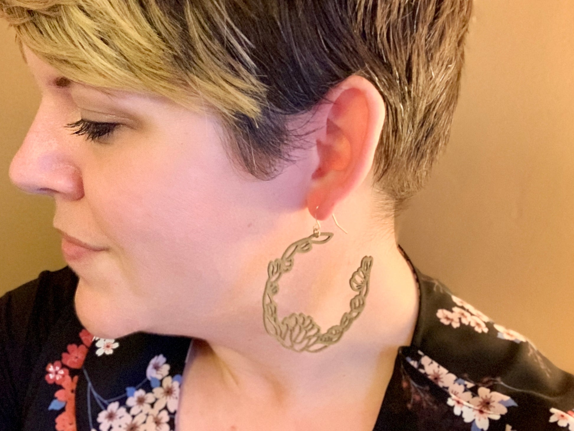 A woman is shown in profile looking away from the camera wearing a R+D 3D printed earring. It is a gold filament with blooms and leaves layered together to form a floral wreath hoop. 