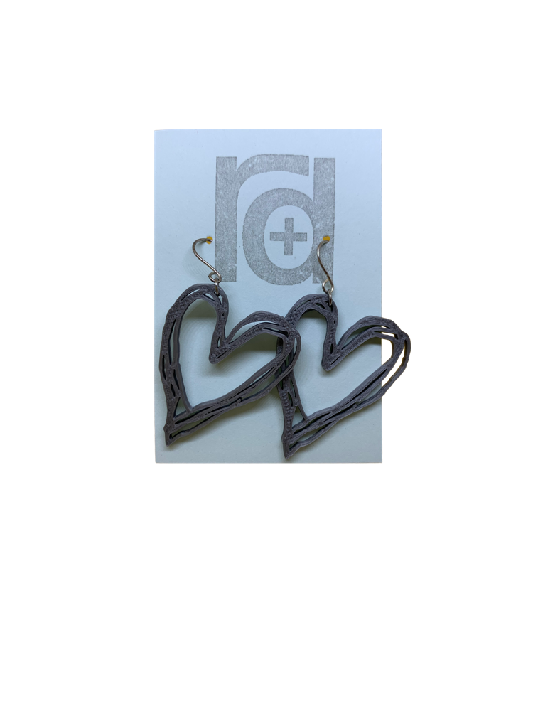 Hanging on a light blue earring card are two heart earrings that are 3D printed from a drawing.