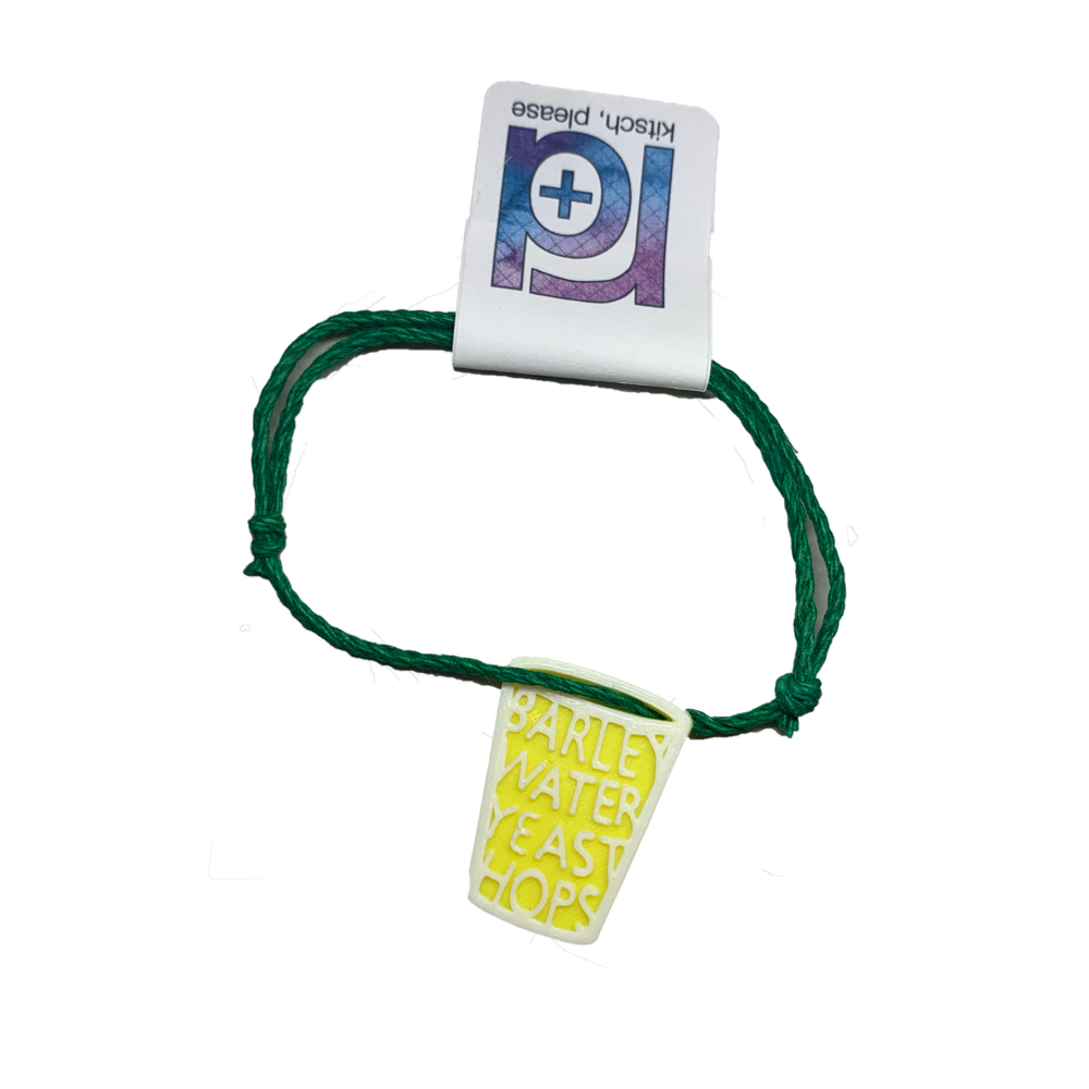 Hanging from a green adjustable bracelet cord is a pint glass with words fit into it. The words are barley, water, yeast, hops; the primary ingredients in beer.
