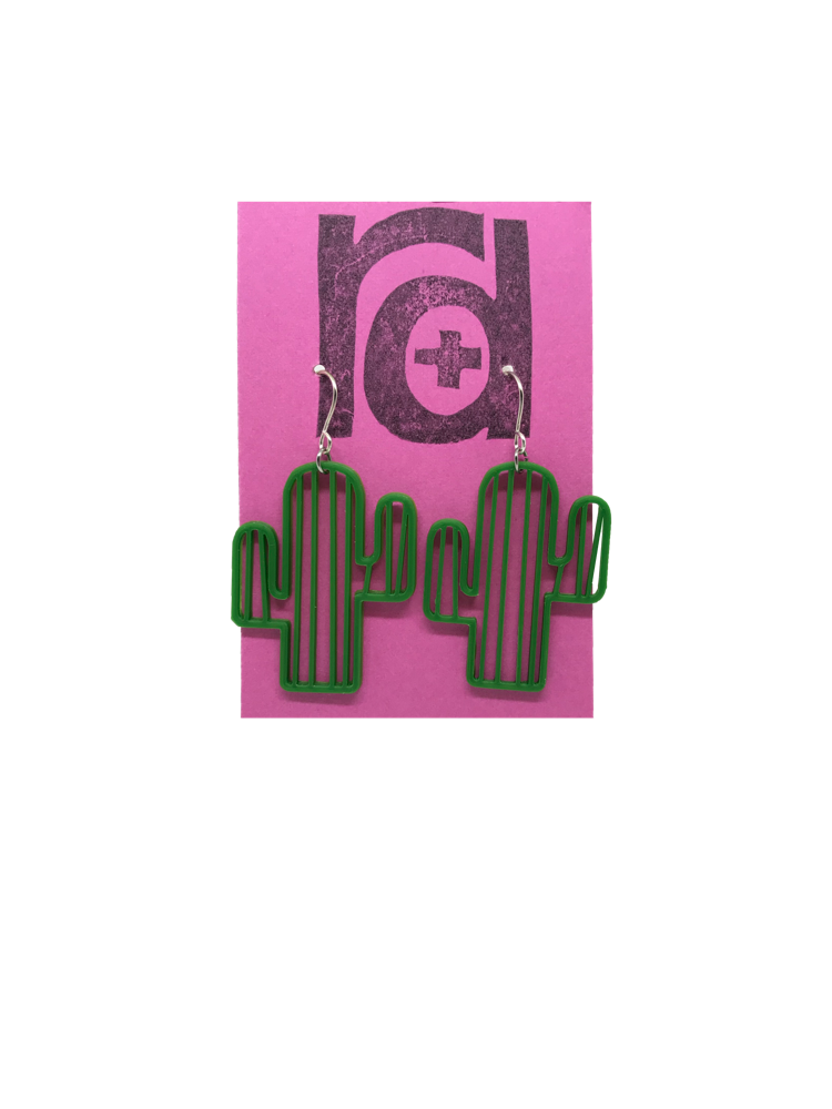 On a bright pink R+D earring card are two 3D printed earrings. They are shaped as cacti with two arms and stripes to give texture. Not only do they look like plants, they are made from plants.