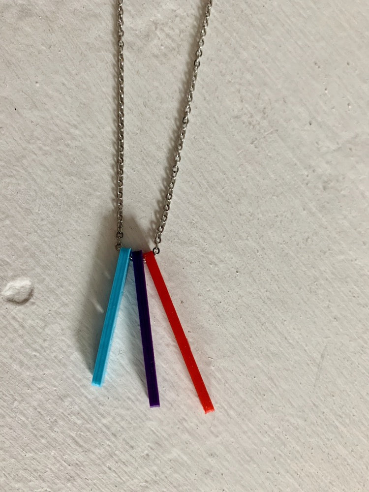On a white background are three 3D printed pendants. They are each different colors and shaped as long rectangles with names in the center. When worn, they simply look like long hanging rectangles, but from the side, all the names are visible. This one has a teal pendant, a purple pendant, and a red pendant.