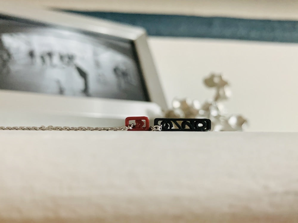 Laying on its side are two 3D printed pendants. One is a dark red merlot color and has a small heart. The other is a black pendant and has 9/20 on it. These pendants can be customized to other names, dates, or words. 