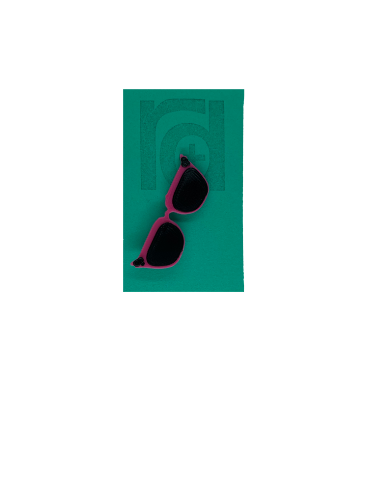 On a teal card is a R+D 3D printed pin. They're in the shape of cat eye sunglasses and have hot pink frames, black lenses, and black accents at the top corners of the glasses.