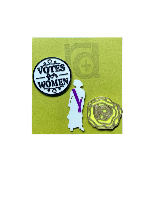 Shown on a green R+D card are a set of three 3D printed pins. The first on the left is a white circle with a black outline and words saying "Votes for Women". The next is a silhouette of a woman from the 1920s. Aside from the silhouette, there is a purple sash. The third pin is a yellow rose, which was worn in support of the movement. The petals are all outlined in gold and in the center is the number 19 for the 19th amendment. 