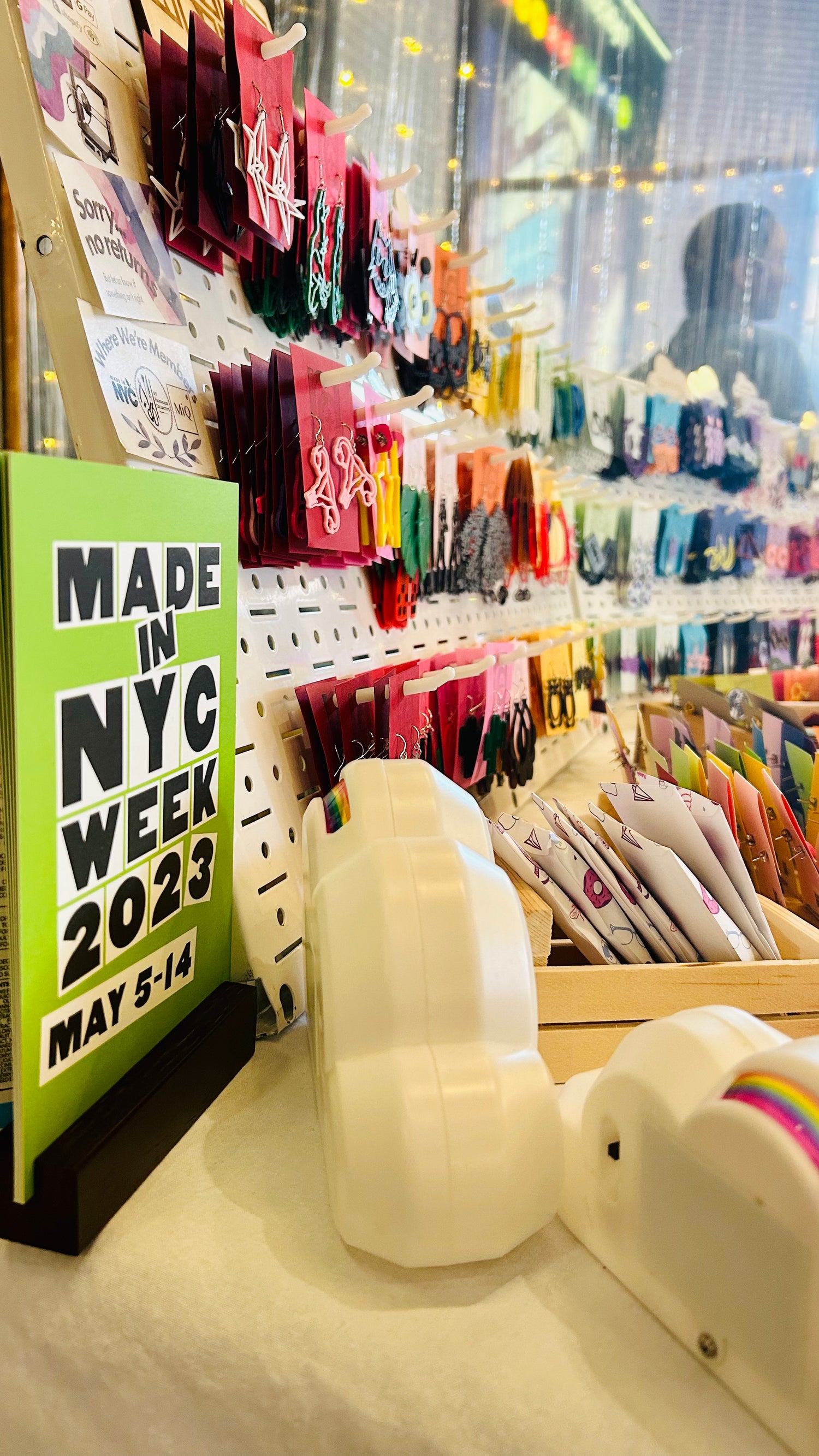 On the edge of a table with a rainbow of hanging earring cards is a bright green card reading Made In NYC Week 2023, which R+D participated in through a partner market.
