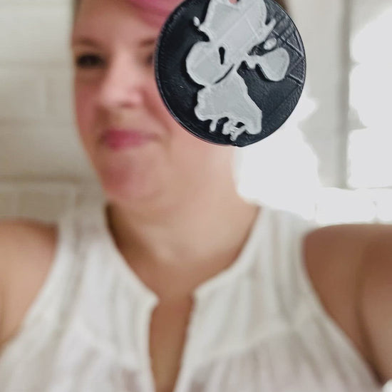 This video starts with a necklace being held close to the camera. It is a black pendant with a paw print in silver. It is customized to any picture of a paw print. In the video the person holding the necklace brings it away from the calendar and puts it on to show how big it is when being worn. 