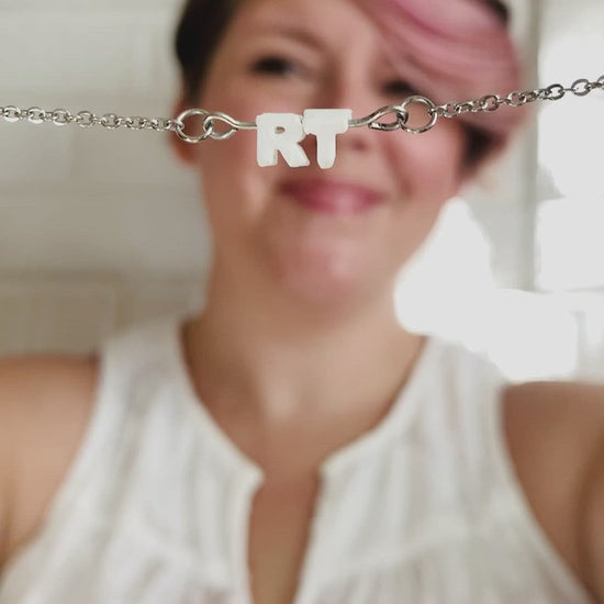 The video starts with Rebekah Thornhill, owner of R+D holding a necklace up to the camera. It has small letters on a metal bar. The letters are like beads and will rotate and move around. This necklace has 2 characters (RT) in a white. In the video she puts the necklace on to show how it looks when being worn.  