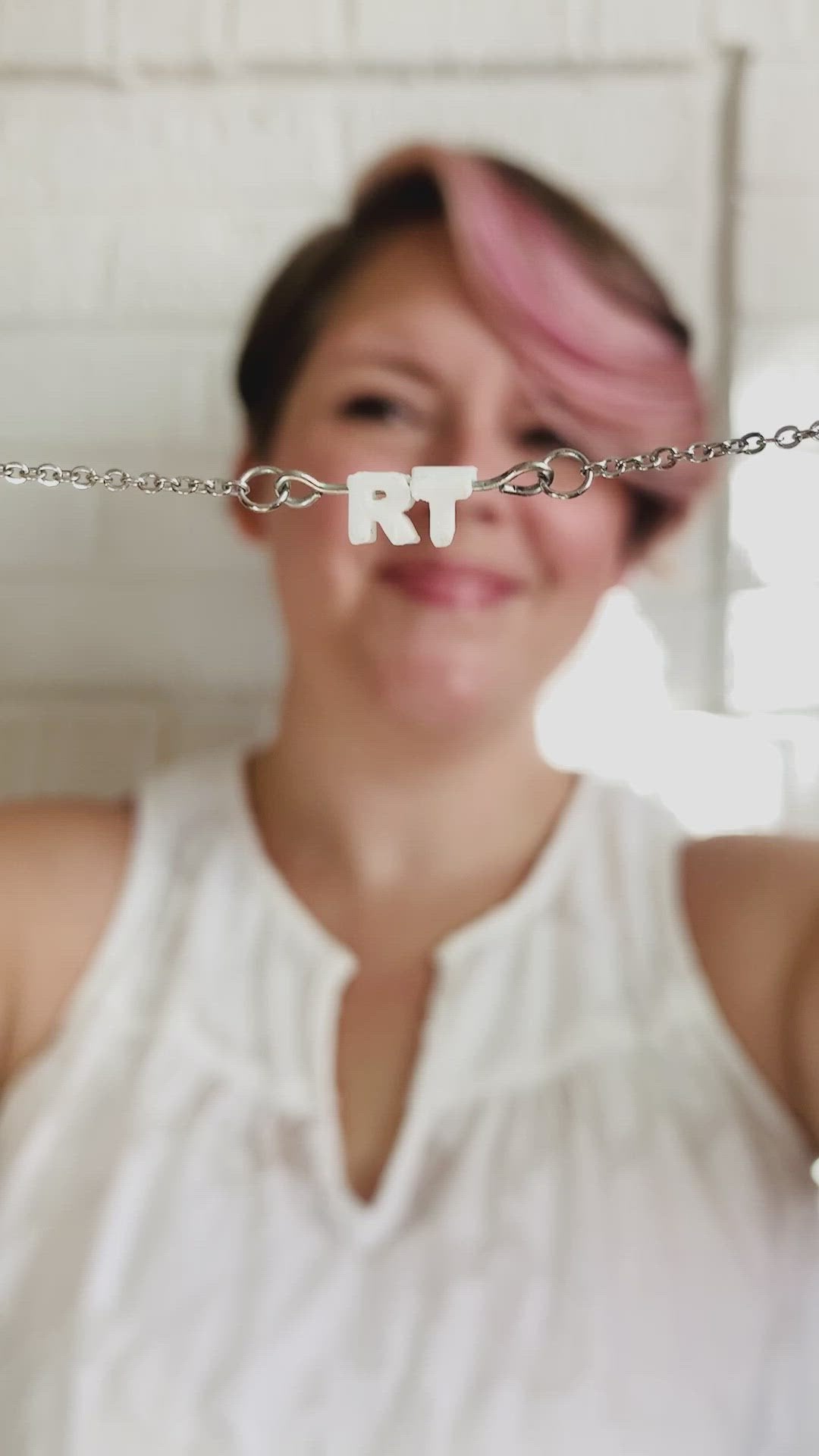 The video starts with Rebekah Thornhill, owner of R+D holding a necklace up to the camera. It has small letters on a metal bar. The letters are like beads and will rotate and move around. This necklace has 2 characters (RT) in a white. In the video she puts the necklace on to show how it looks when being worn.  