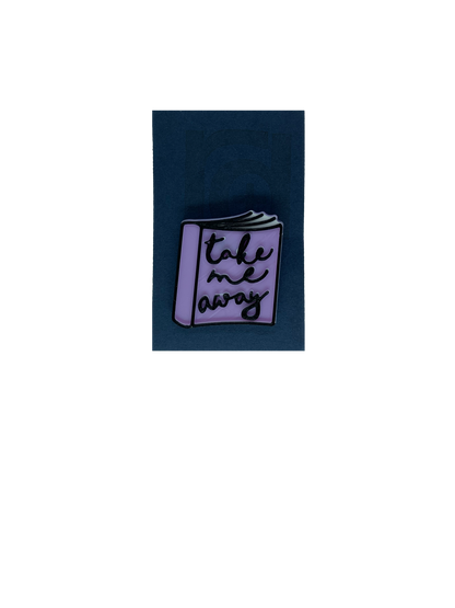 On a dark blue card is a 3D printed pin. It is the shape of a  paper back book. IThe books light purple, with white pages and has details outlined in black. On the cover, it reads, Take me away in a scripted cursive font.