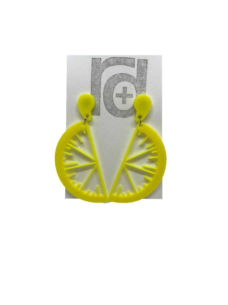 On a white paper earring card are two R+D earrings. They are two slices of fruit hanging from drops of fruit juice. These are yellow like bright lemons.