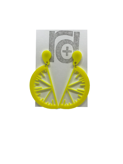 On a white paper earring card are two R+D earrings. They are two slices of fruit hanging from drops of fruit juice. These are yellow like bright lemons.