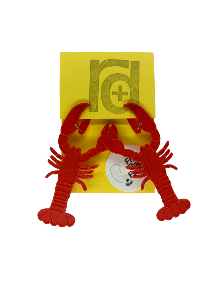 Hanging off of a bright yellow earring card are two striking red lobster earrings. The larger crusher claw is designed to look like it is pinching around the earlobe when being worn.