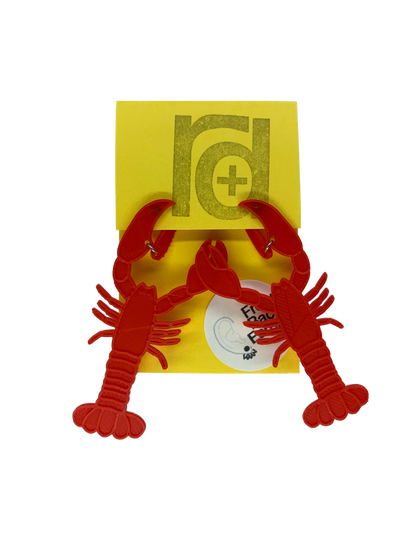 Hanging off of a bright yellow earring card are two striking red lobster earrings. The larger crusher claw is designed to look like it is pinching around the earlobe when being worn.