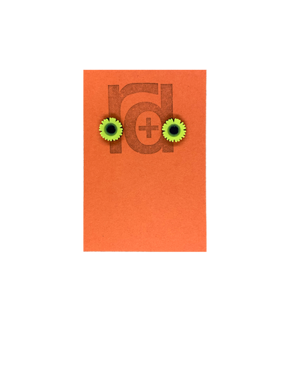 On a orange earring tag are two small and detailed  R+D studs. They are  shaped as sunflowers with black centers and bright yellow petals all around.
