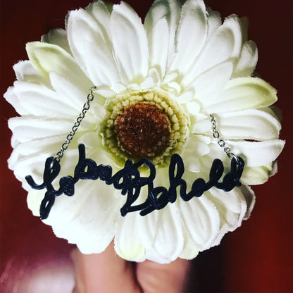 There is a large daisy with a necklace in the middle. The necklace has a 3D printed pendant made from a sample of handwriting.