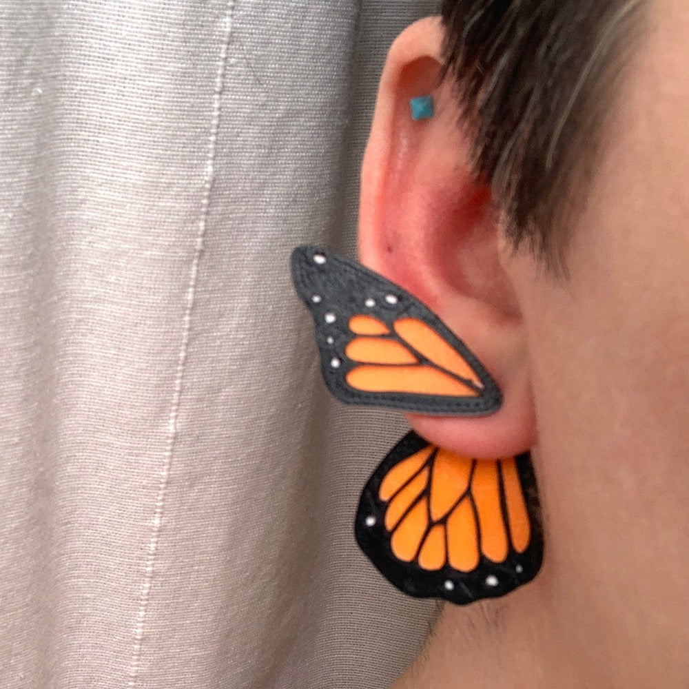 This is a close up of a butterfly wing earring -- the smaller wing is worn on the front of the earlobe and the larger wing hangs behind the earlobe. These R+D earrings are 3D printed with plant based materials. 