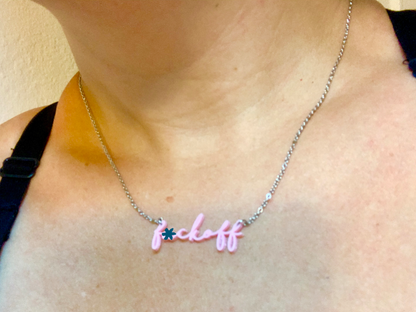 Shown being worn is a 3D printed pendant necklace. In a modern cursive script it says f*ck off in a light pink color.