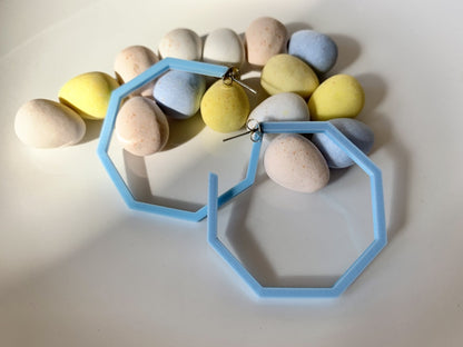 Two light blue hexagon hoops are laying over a handful of candy coated eggs for spring. The hoops are 3D printed with a plant based material.