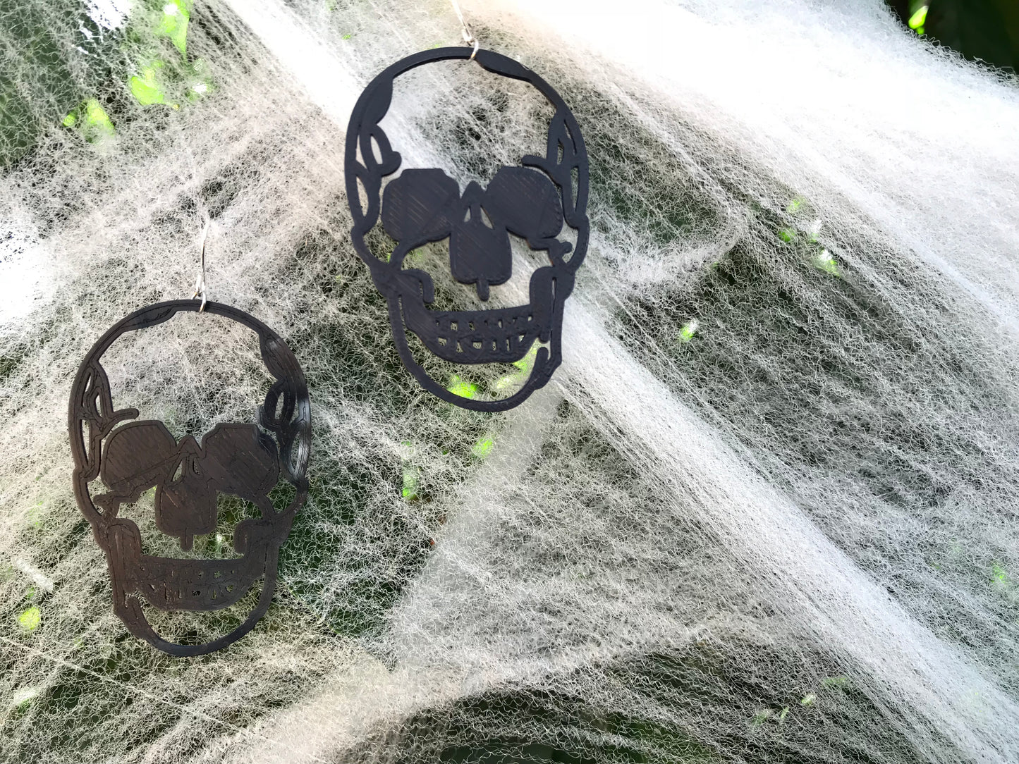 Hanging off of fake cobwebs for Halloween are two large black skull earrings. They are realistic in their shape and could be considered edgy or creepy.