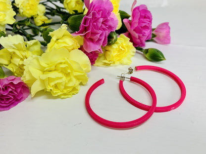 In the background are yellow and pink carnations. Laying in front of them are two hot pink 3D printed hoops. 