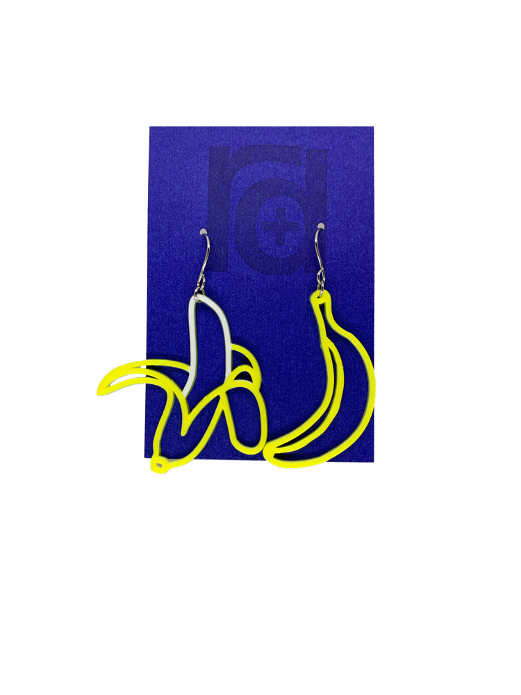 On a bright blue earring card that is the same color as the Chiquita Banana stickers, hang two R+D 3D Printed earrings. They are asymmetrical styles, but both bananas. One is a bright unpeeled, yellow  banana and the other has the skin pulled down to reveal a white banana.