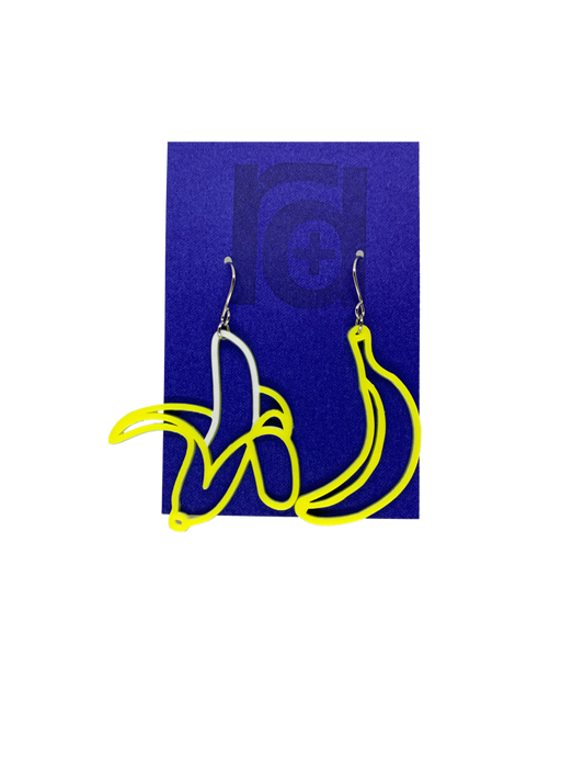 On a bright blue earring card that is the same color as the Chiquita Banana stickers, hang two R+D 3D Printed earrings. They are asymmetrical styles, but both bananas. One is a bright unpeeled, yellow  banana and the other has the skin pulled down to reveal a white banana.