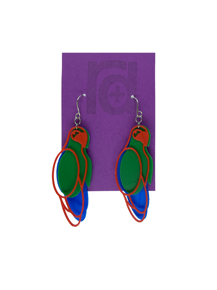 Hanging from a bright purple earring card are two R+D 3D printed earrings. The earrings each have three pieces that form a parrot shape that is red, green, and blue.
