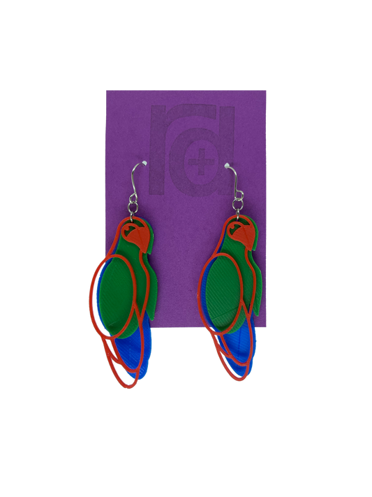 Hanging from a bright purple earring card are two R+D 3D printed earrings. The earrings each have three pieces that form a parrot shape that is red, green, and blue.