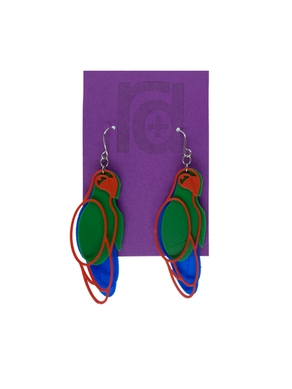 Hanging from a bright purple earring card are two R+D 3D printed earrings. The earrings each have three pieces that form a parrot shape that is red, green, and blue.