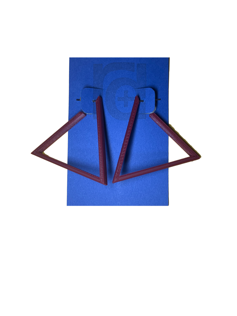 Hanging off of a blue R+D earring card are two 3D printed earrings. They are hoops that are in the shape of a triangle. These earrings are printed in a eco friendly deep red merlot.