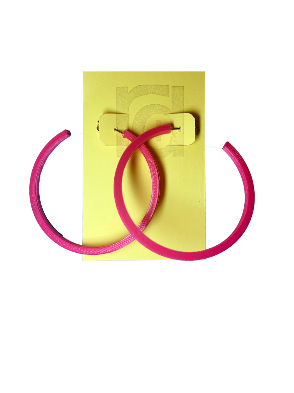 Shown on a yellow R+D card are two 3D printed hoop earrings. They are large two inch hoops in a bright hot pink  that are lightweight and plant based.