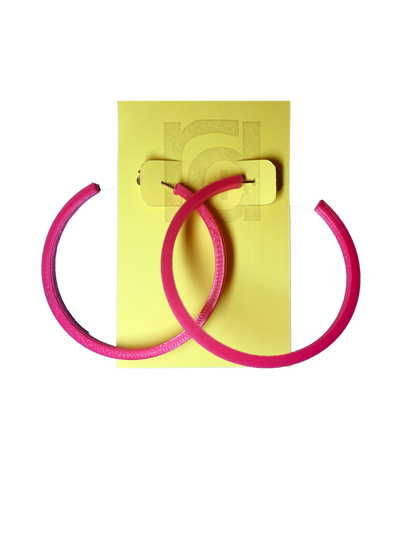 Shown on a yellow R+D card are two 3D printed hoop earrings. They are large two inch hoops in a bright hot pink  that are lightweight and plant based.