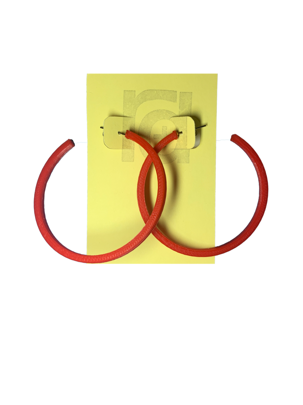 Shown on a yellow R+D card are two 3D printed hoop earrings. They are large two inch hoops in a bright red that are lightweight and plant based. 