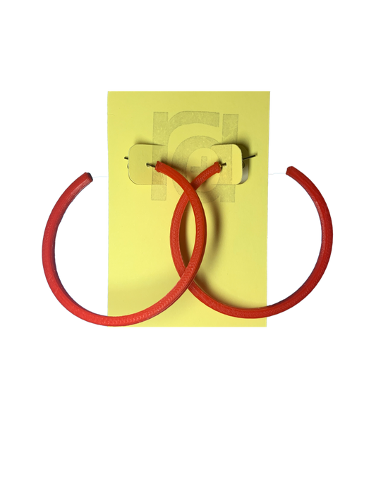 Shown on a yellow R+D card are two 3D printed hoop earrings. They are large two inch hoops in a bright red that are lightweight and plant based. 