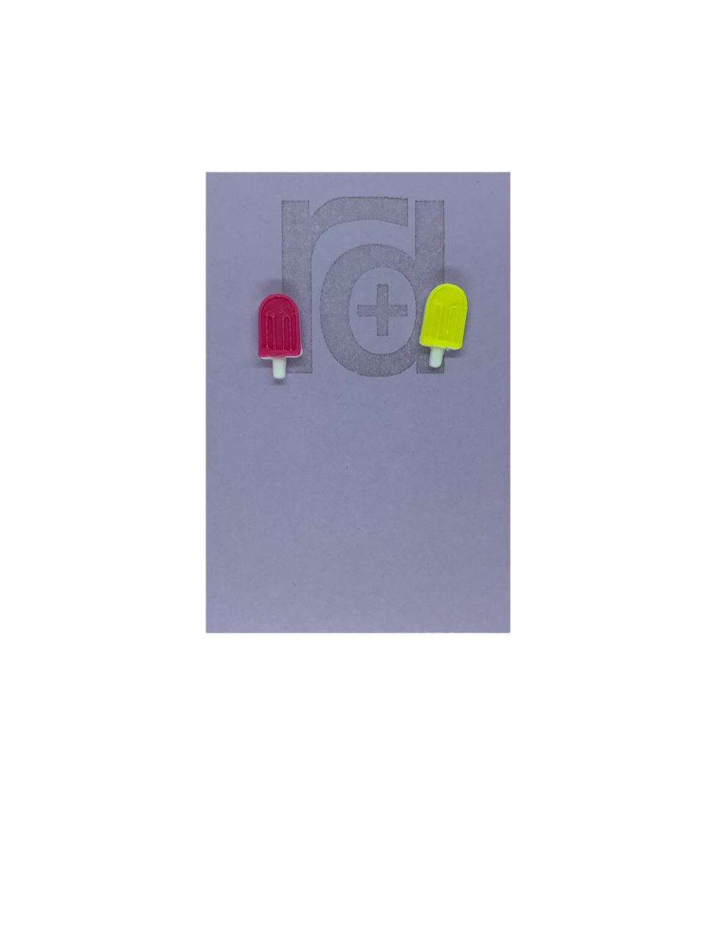 Two small and detailed R+D earrings are shown on a purple earring card. They are shaped as popsicles with white sticks. The earrings are mismatched, one popsicle is hot pink and one is bright yellow.
