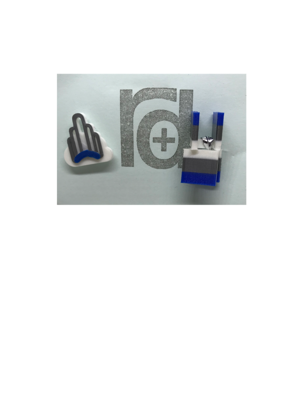 Shown on a small light blue card is a 3D Printed pin next to a set of cufflinks. The pin has a white cloud with a silver and blue art deco arch in front.  This arch is a prominent landmark in the Sunnyside neighborhood in Queens, NY. The cufflinks are squares that have the same white, blue, and silver colors  of the arch in horizontal stripes. 