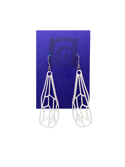 Hanging off of a bright blue earring card are two earrings. They are white and show a delicate wing of a dragonfly or insect with all the veins.