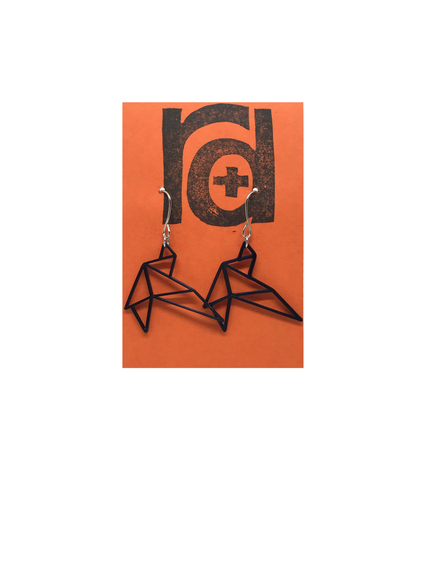 Shown on a bright orange earring card are two R+D earrings. They are geometric line shapes of birds flying. These sustainable 3D printed earrings are printed in black.