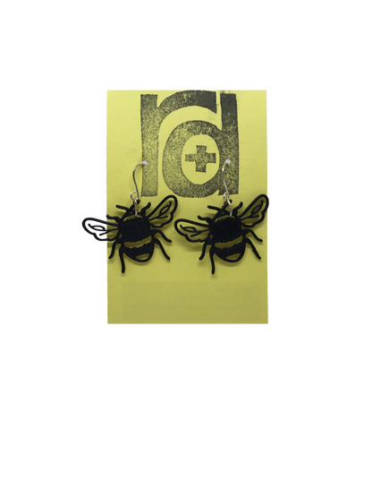 On a muted yellow card are two R+D earrings. They are shaped like bumble bees straight on; they have delicate veins in the wings and the body includes the quintessential stripes of a bee that are fuzzy for collecting pollen.