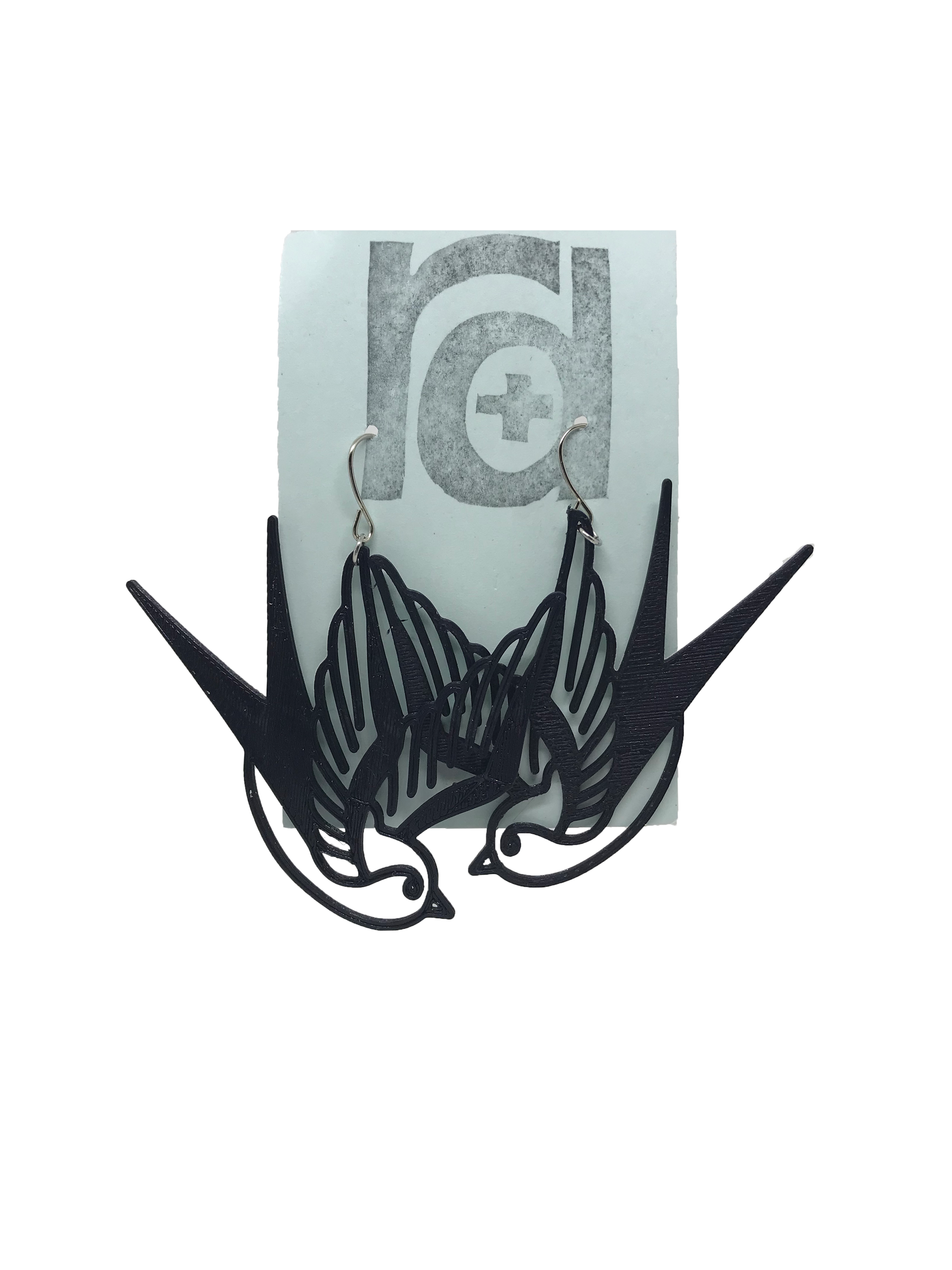 On a light blue earring card are two R+D earrings. They are black and look like two swallow birds that are circling or flying down.