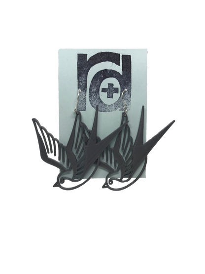 On a light blue earring card are two R+D earrings. They are an eco friendly silver and look like two swallow birds that are circling or flying down.