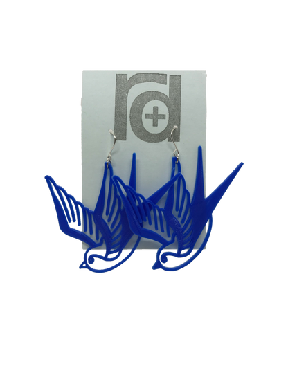 On a light blue earring card are two R+D earrings. They are a classic cobalt blue and look like two swallow birds that are circling or flying down.