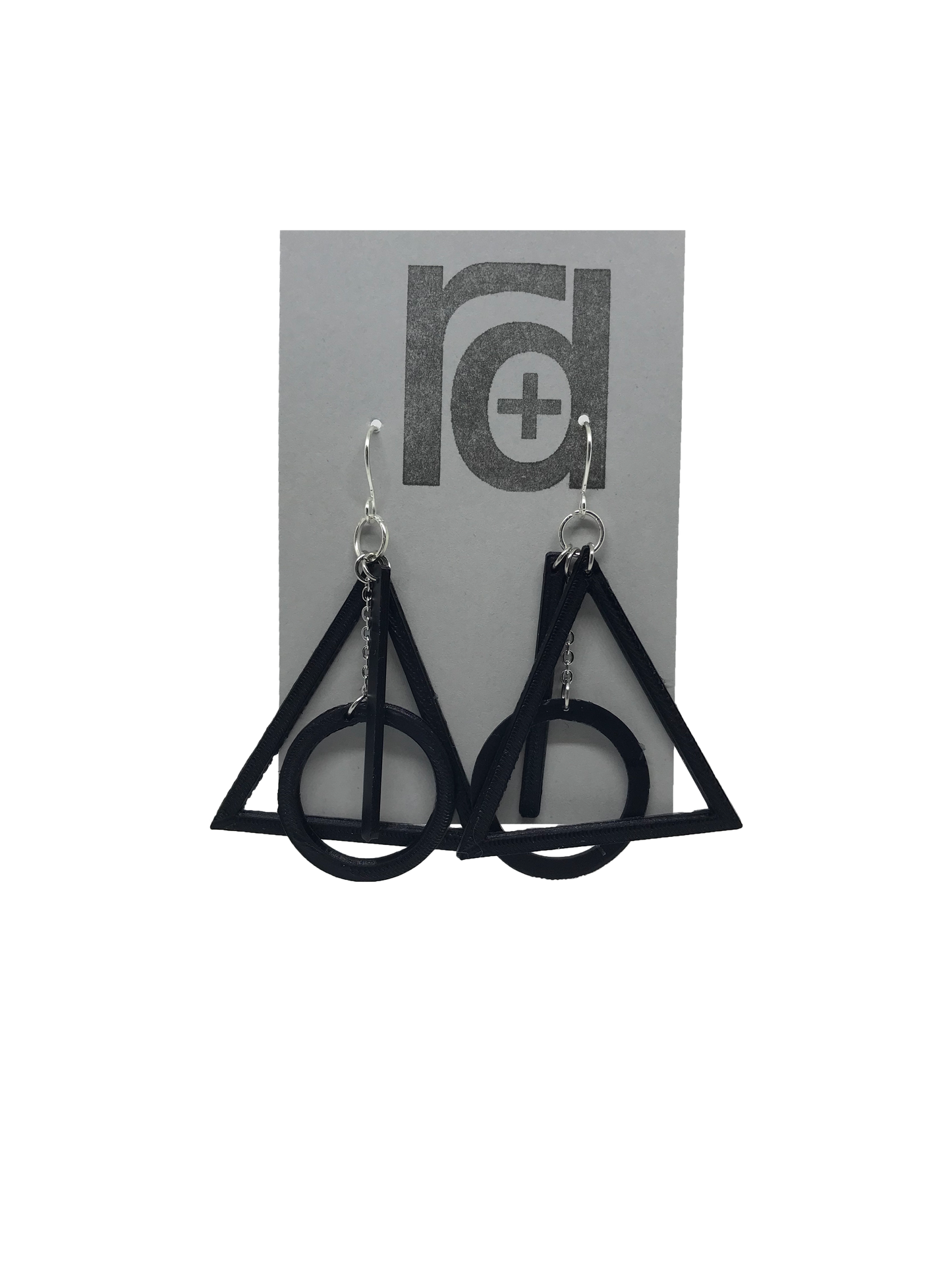On a grey earring card are two R+D earrings. They are based off of a symbol from a popular book series. There is a black triangle, a circle, and a line that all move independently but come together to make one the master of death. 