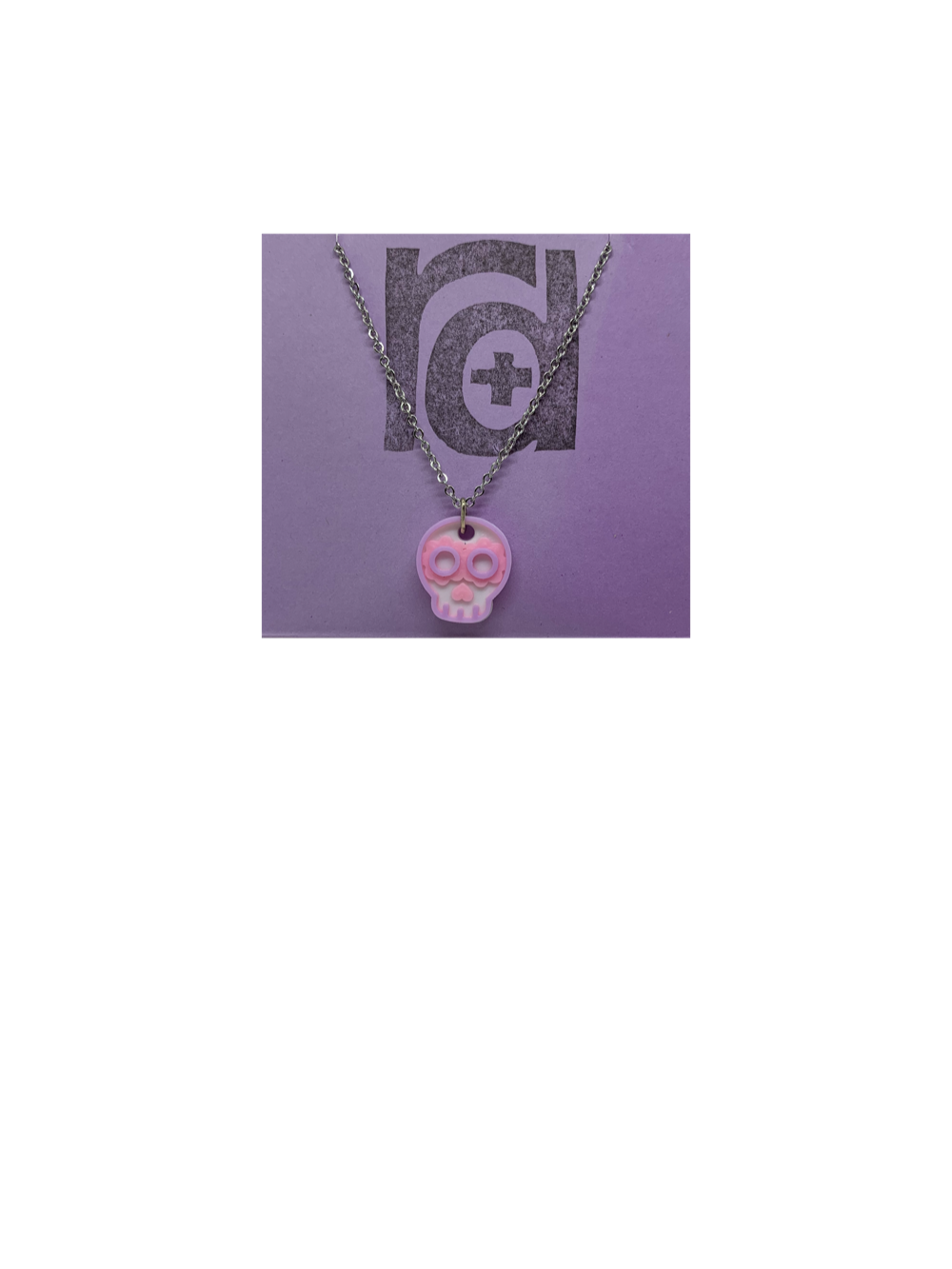 Shown on a light purple R+D earring card is a necklace with a sugar skull pendant. The small pendant is 3D printed in 3 colors: white, light pink, and light purple.