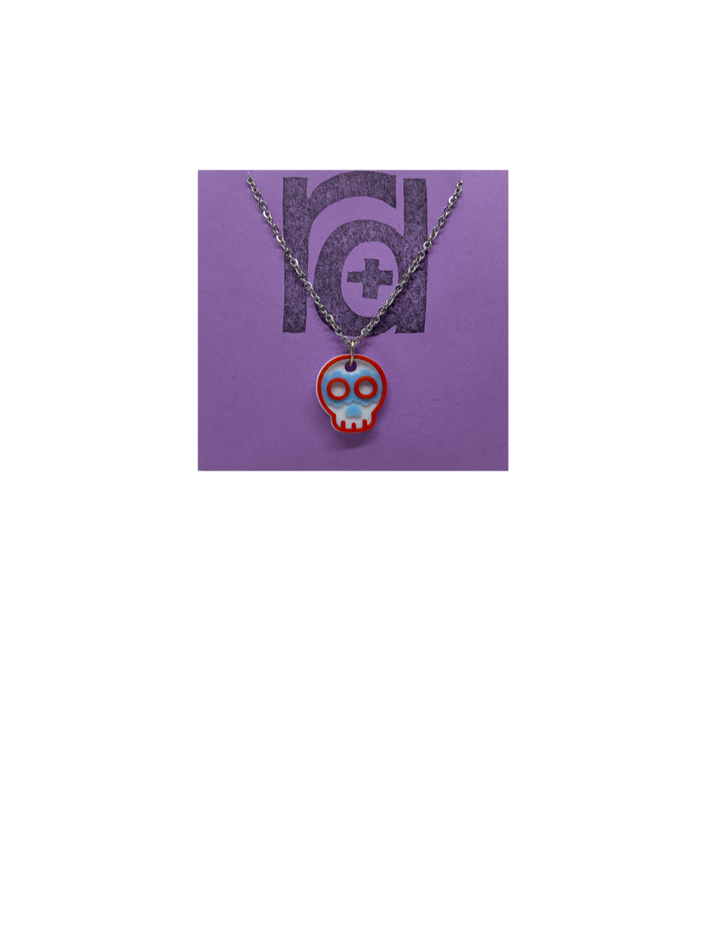 Shown on a light purple R+D earring card is a necklace with a sugar skull pendant. The small pendant is 3D printed in 3 colors: white, light blue, and red. 