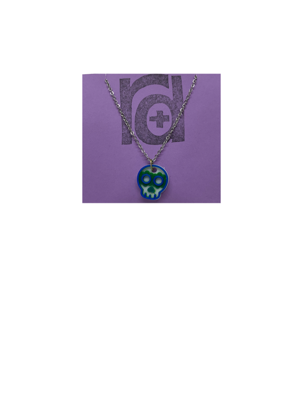 Shown on a light purple R+D earring card is a necklace with a sugar skull pendant. The small pendant is 3D printed in 3 colors: white, green, and blue.