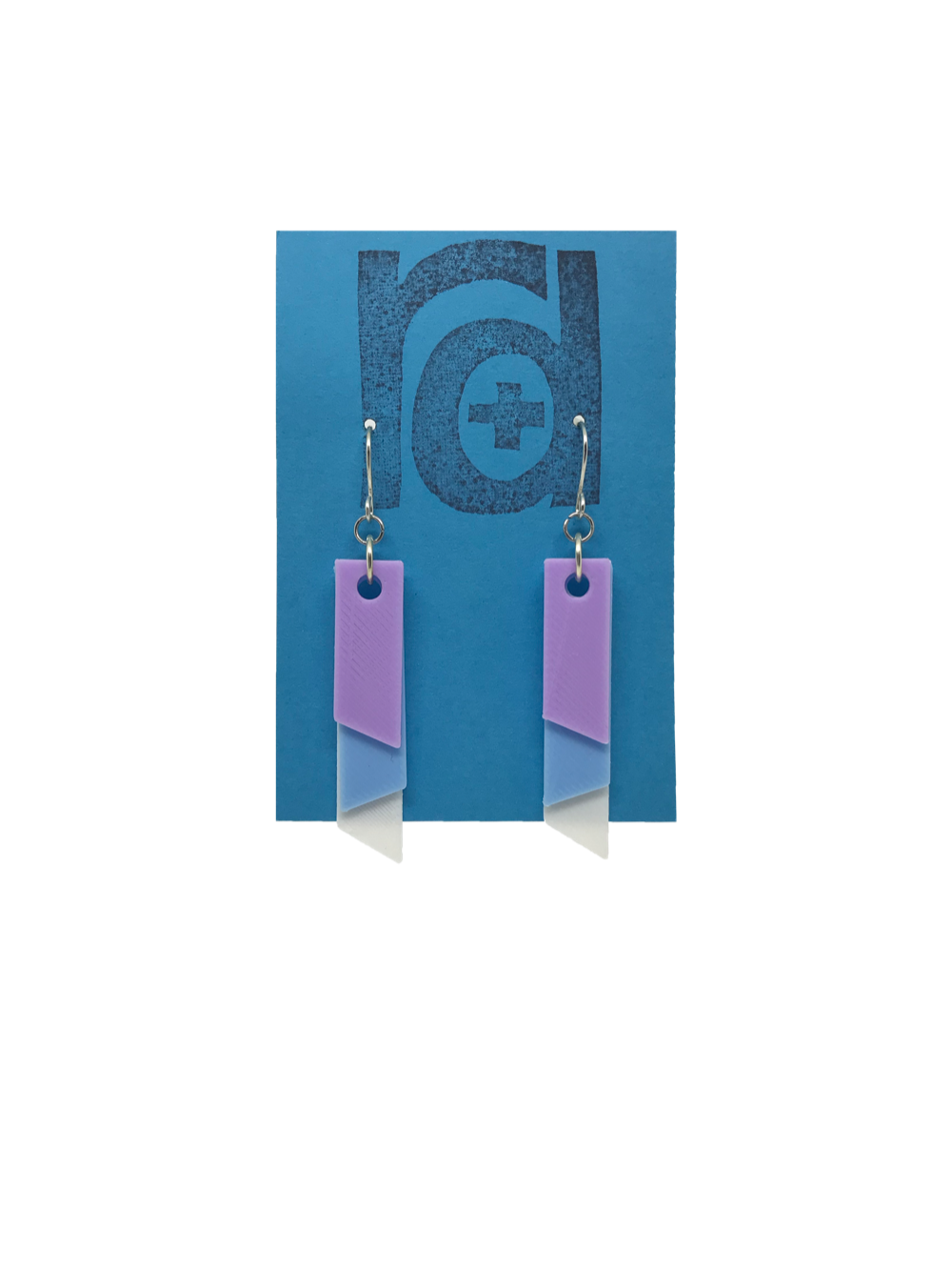 On a bright blue R+D earring card is a set of 3D printed earrings. The  earrings are 3D printed with a plant based filament to make them sustainable as well as affordable. There are three banners hanging down; one is white, one is light blue, and the final is light purple. They are each different lengths so that the colors show. 