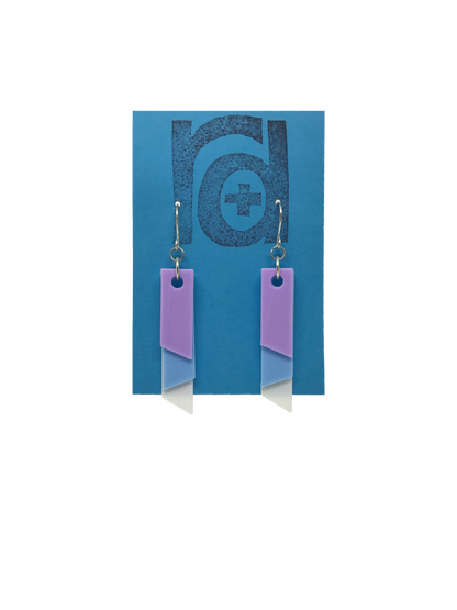 On a bright blue R+D earring card is a set of 3D printed earrings. The  earrings are 3D printed with a plant based filament to make them sustainable as well as affordable. There are three banners hanging down; one is white, one is light blue, and the final is light purple. They are each different lengths so that the colors show. 