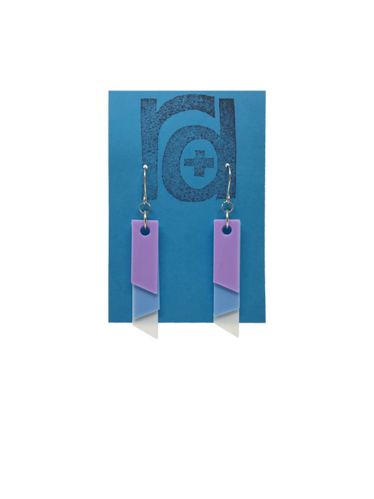 On a bright blue R+D earring card is a set of 3D printed earrings. The  earrings are 3D printed with a plant based filament to make them sustainable as well as affordable. There are three banners hanging down; one is white, one is light blue, and the final is light purple. They are each different lengths so that the colors show. 